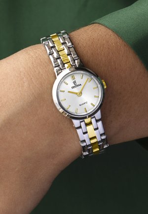 Polshorloge met een zilver- en goudkleurige metalen band, witte ronde wijzerplaat, gouden uurmarkeringen en wijzers, die de tijd 10:10 aangeeft op een pols met een groene mouw.