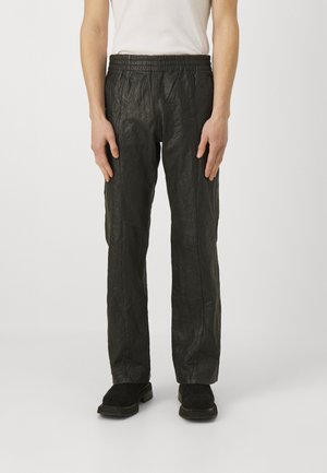 Pantalones negros texturizados con cintura elástica, corte recto y acabado arrugado; llevados con calzado negro.