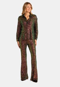 Conjunto de lentejuelas que incluye una blusa con cuello y pantalones acampanados en tonos arcoíris, con una superficie texturada y reflectante y mangas largas.