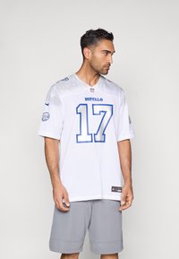 Balta NFL spēļu krekls ar zilām detaļām un numuru 17, virs kura ir uzraksts "BUFFALO". Valkāts kopā ar pelēkām šortiem. Īsām piedurknēm, apaļa kakla izgriezums.