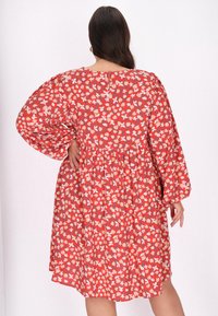 Rochie roșie cu flori, cu mâneci lungi și umflate și o croială lejeră. Prezintă o talie adunată și un nasture la gât în spate.