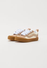 Brązowe i kremowe sneakersy z białymi sznurówkami, wykonane z zamszu i płótna, o zaokrąglonym nosku, z gumową podeszwą, z kontrastowym paskiem po boku oraz naszywką na pięcie.