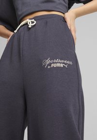 Pantaloni da jogging grigio scuro realizzati in materiale morbido con vita regolabile tramite cordino. Presentano la scritta "Sportswear by PUMA" ricamata in crema chiaro.