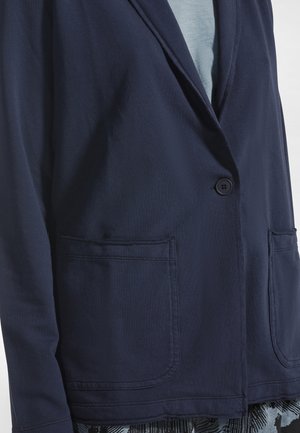 Blazer bleu marine en tissu lisse, avec une fermeture à un bouton, des revers crantés et deux poches avant.