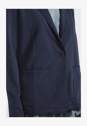 Blazer azul marino de tela suave, con cierre de un solo botón, solapas con muesca y dos bolsillos delanteros.