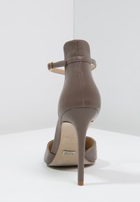 Chaussure à talon haut marron avec un bout pointu, une sangle à la cheville et une texture en cuir lisse. Présente un talon stiletto étroit et un détail de logo sur la semelle.