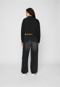 Svart kort hettegenser kombinert med løse, falmede svarte denimjeans. Antrekket har et enkelt design og en uformell stil.