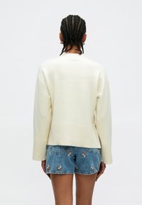 Kremfarget strikkegenser med løs passform og ribbestrikket kant, kombinert med denimshorts med blomsterbroderi og frynsete kant.