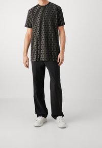 Svart t-shirt med vitt vertikalt textmönster, rund halsringning, korta ärmar, tillsammans med svarta byxor och vita sneakers.