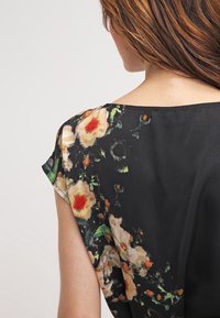 Blusa negra con estampado floral de manga corta. Presenta un patrón floral en tonos de naranja, rosa y verde sobre un fondo oscuro. Textura suave.