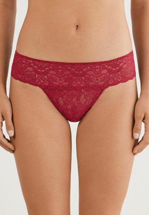 Tanga en dentelle rouge profond avec un motif floral. Présente une taille en dentelle festonnée et un tissu lisse pour le confort.