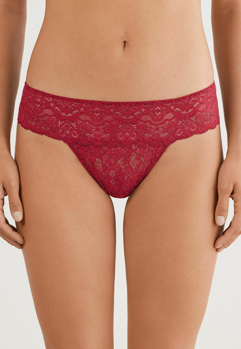 Tanga en dentelle rouge profond avec un motif floral. Présente une taille en dentelle festonnée et un tissu lisse pour le confort.