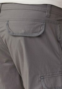 Nahaufnahme von grauen Cargo-Hosen mit einer Klappentasche auf der Rückseite und einem kleinen Stoffetikett an der Seite.