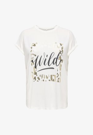 Joven con el pelo largo que lleva una camiseta blanca con estampado "wild", pantalones cortos negros con dobladillo festoneado, sandalias negras y pulseras en la muñeca.