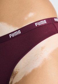 Bordeaux katoenen bikini met een witte PUMA logo tailleband. Het materiaal is glad met een aansluitend design, waardoor de huidtinten zichtbaar zijn.