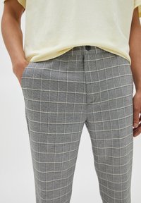 Pantaloni a quadri grigi realizzati in tessuto testurizzato, con un motivo a griglia e sottili linee beige, tasche anteriori e chiusura con bottone.