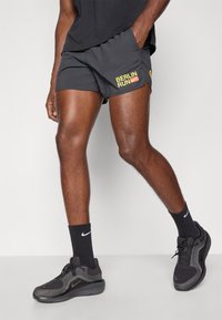 Czarne spodenki sportowe z żółtym napisem "BERLIN RUN", kieszeń boczna oraz czarne buty Nike z teksturowaną cholewką i amortyzującą podeszwą. Czarne skarpetki do kostek.