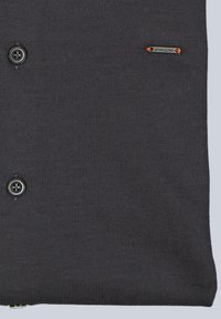 Grau gestrickter Stoff mit zwei schwarzen Knöpfen und einem kleinen orangefarbenen Emblemlabel. Glatte Textur mit einem schlichten Design und ohne sichtbare Muster.