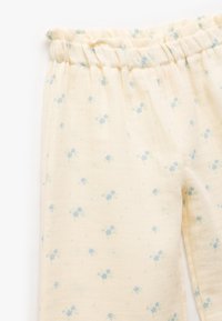 Pantalones con estampado floral en tela color crema claro con cintura elástica. Presenta pequeños flores azules y acentos verdes en toda la tela.