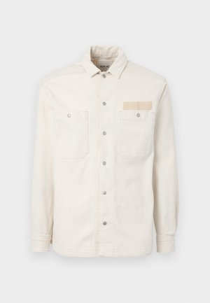 White denim jacket featuring long sleeves, a point collar, two front pockets, metal snap buttons, and a branded fabric label on the chest.
