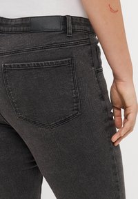 Jeans de mezclilla negra con un corte slim, un bolsillo trasero con costuras visibles y una etiqueta de marca de cuero en la cinturilla.