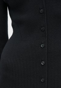 Λεπτομέρεια μαύρου πλεκτού πουλόβερ με εφαρμοστή σχεδίαση, υφή υφάσματος και έξι κουμπιά που ταιριάζουν κατά μήκος του εμπρός μέρους.