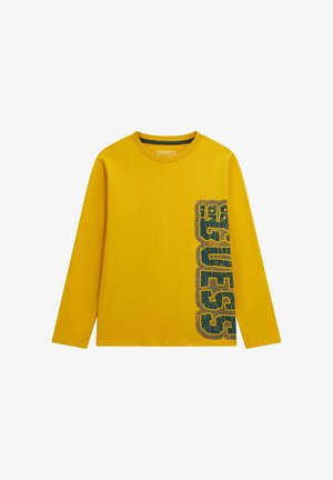 Gelbes Langarm-T-Shirt mit "GUESS" in verblassten schwarzen Buchstaben vertikal auf der rechten Seite bedruckt.