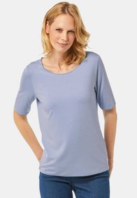 Helles blaues Kurzarm-Oberteil aus weichem Material, mit rundem Ausschnitt und lockerer Passform. Kombiniert mit blauen Jeans.