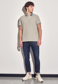 Ljusgrå polo t-shirt med kontrasterande mörkblå krage och ärmslut, kombinerad med mörka denimjeans och beigefärgade sneakers.