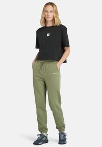 Schwarzes, kurz geschnittenes T-Shirt mit kleinem Logo, kombiniert mit olivgrünen Jogginghosen mit elastischem Bund und Timberland-Branding.