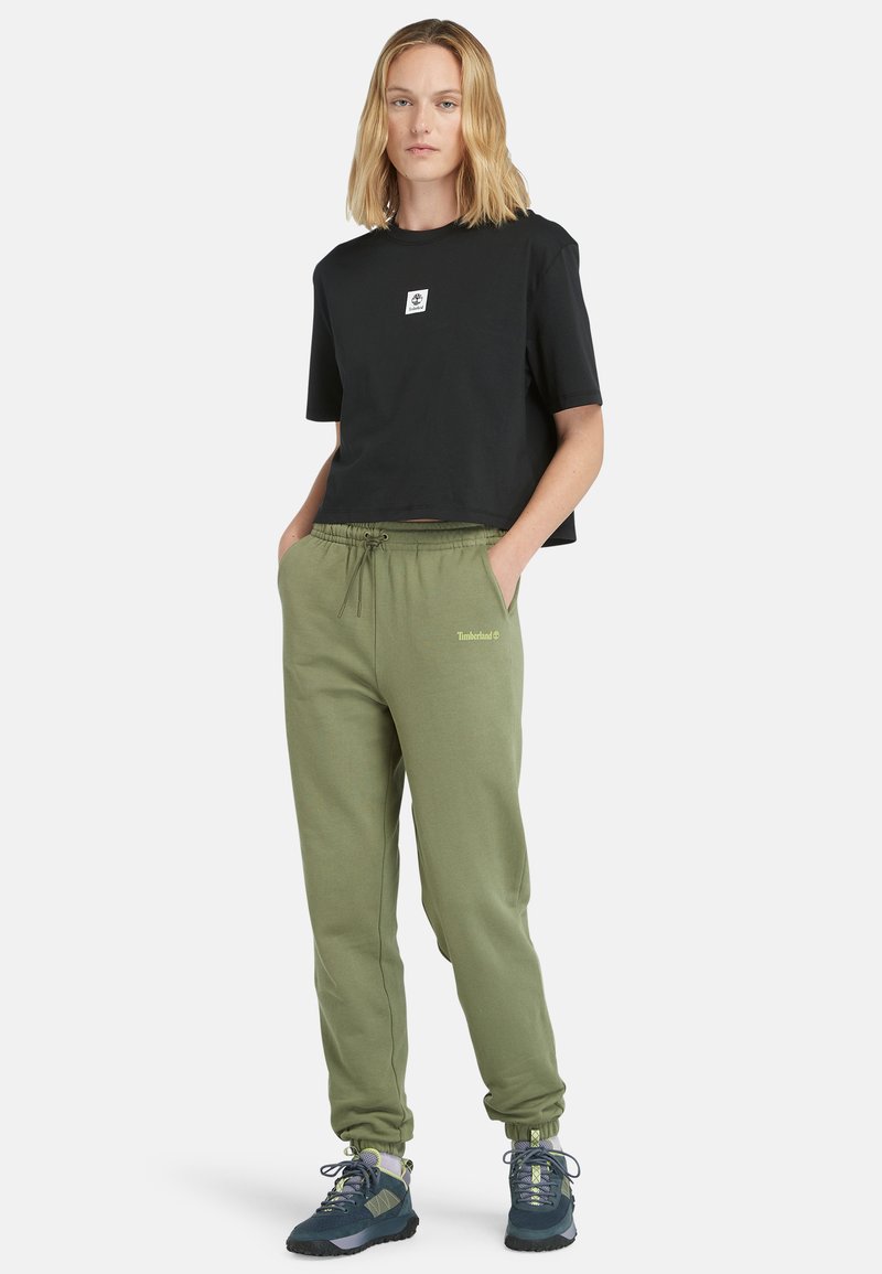 Schwarzes, kurz geschnittenes T-Shirt mit kleinem Logo, kombiniert mit olivgrünen Jogginghosen mit elastischem Bund und Timberland-Branding.