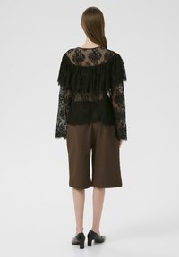 Sort blonderet top med flæseærmer, parret med brune culottes. Blonden har et blomstermønster og en gennemsigtig tekstur. Sorte hæle fuldender looket.