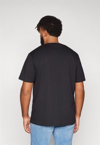 Schwarzes Baumwoll-T-Shirt mit Rundhalsausschnitt und kurzen Ärmeln, geradem Saum und minimaler Detailgestaltung. Getragen mit hellblauen Jeans.
