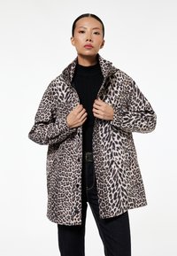 Jasje met luipaardprint, hoge kraag, lange mouwen en zijzakken. De stof lijkt zacht met een gestructureerde, glanzende afwerking.