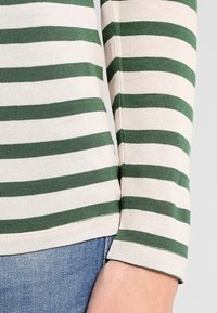 Long-sleeve T-shirt featuring horizontal green and cream stripes, with a soft cotton texture and a simple round neckline.