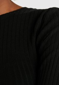 Svart ribbat tyg med ett texturerat mönster. Plagget har en rund halsringning och en något puffad axeldesign.