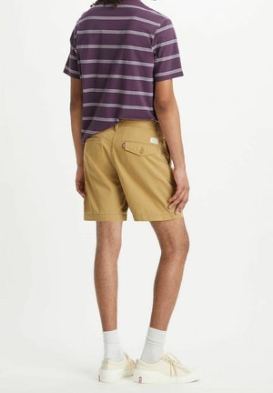 Khaki shorts med sidelommer og en baglomme med lap. Kombineret med en lilla stribet kortærmet skjorte. Hvide sneakers og crew-sokker.