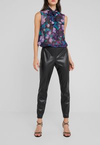 Blusa senza maniche viola a fiori con dettaglio a fiocco, abbinata a pantaloni in pelle neri aderenti e sandali con tacco a strappo.