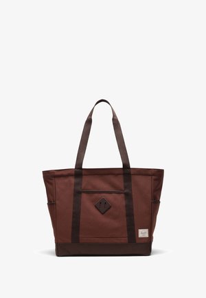 Brown canvas tote bag with dark brown accents, featuring two shoulder straps, a diamond-shaped patch, and a front pocket.