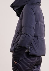 Chaqueta de plumas azul marino con cuello alto, textura acolchada y bolsillos laterales, combinada con pantalones rayados en blanco y negro.
