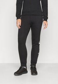 Svart bomullssvetter har en slim fit med ribbede mansjetter, logo-detalj på siden, og er kombinert med svarte joggesko.