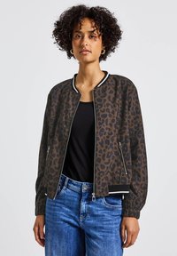 Bomber bunda s leopardím potiskem v hnědé a černé barvě, s žebrovanými manžetami a spodním lemem; zapínání na zip, s bočními kapsami a jednoduchým černým tričkem pod ní.