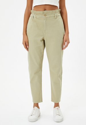 Pantalones de tiro alto en verde claro, con un corte relajado, pierna estrecha y sutiles pliegues en la cintura. Combinados con zapatillas blancas.