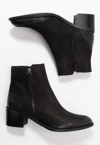 Botas negras hasta el tobillo hechas de cuero suave, con un cierre lateral, punta redondeada y tacón apilado. El diseño presenta una silueta elegante.