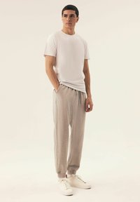 Weißes T-Shirt mit kurzen Ärmeln kombiniert mit hellgrauen Jogginghosen, die über einen elastischen Bund und Bündchen verfügen, ergänzt durch weiße Sneakers.