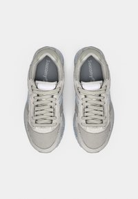 Graue Sportschuhe mit einem Obermaterial aus Mesh, Schnürdesign, strukturierten Details und hellblauen Akzenten an der Sohle. Logo auf der Zunge sichtbar.