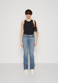 Top con righe nere, jeans svasati blu chiaro, sneakers bianche e una piccola borsa nera. La persona indossa occhiali da sole ed è in piedi frontalmente.