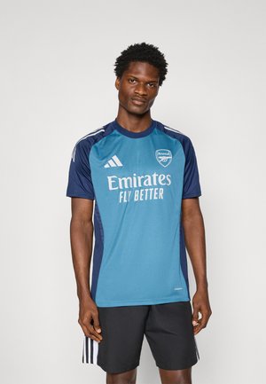 Teal og marineblå kortærmet trøje med "Emirates Fly Better" logo og Arsenal mærke. Har tre hvide striber på skuldrene.
