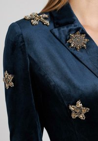 Donkerblauwe fluwelen blazer met versierde ster broches op de schouders, met ingewikkelde bead- en juweelontwerpen. Dankzij de gladde textuur heeft het een luxe uitstraling.