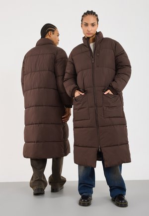 Brown padded long coat with a high collar, side pockets, and vertical seams. Zipper closure visible; modeled on two individuals from front and back.
